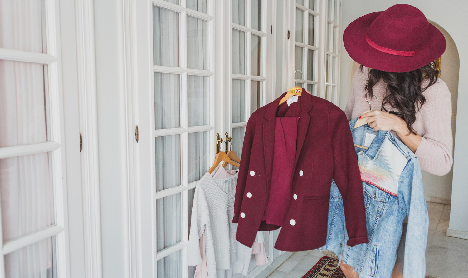 Woman in a burgundy hat choosing between a blazer and a denim jacket, getting dressed with intention